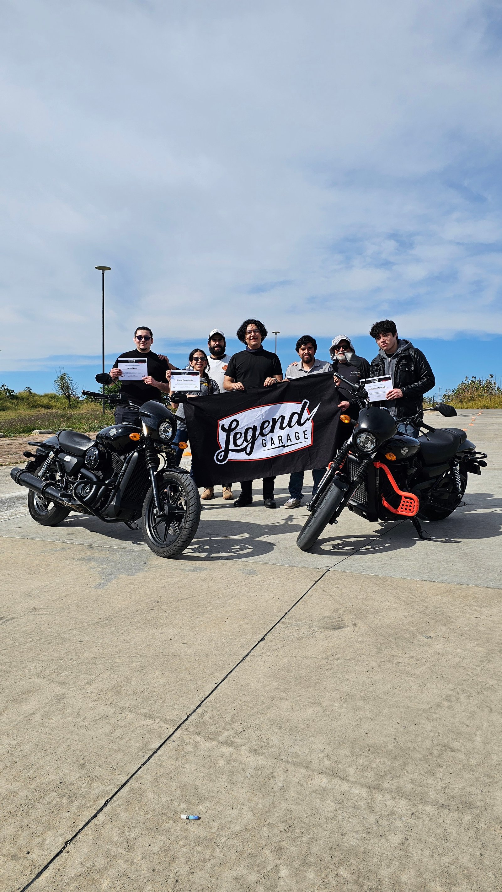 Alumnos de Riding Academy con motocicletas y banner de Legend Garage